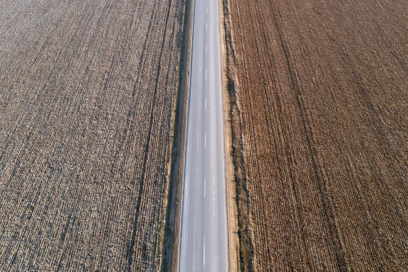 Straight two-lane asphalt road cutting through harvested fields from above