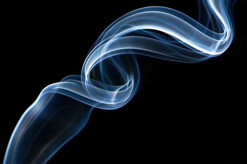 Thin wisp of incense smoke curling into a looping swirl against black background
