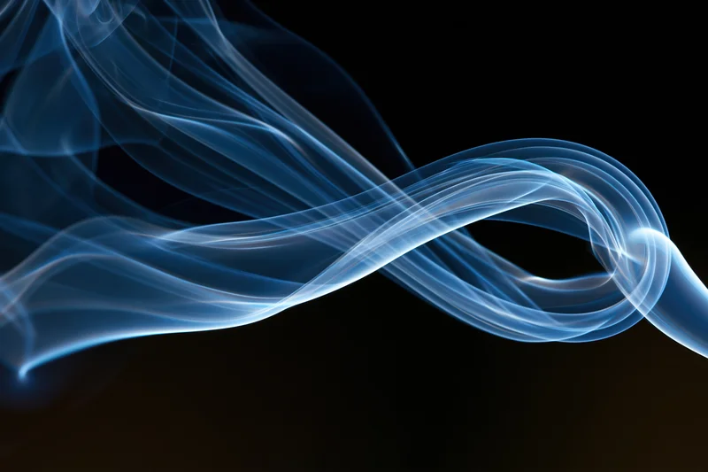 Thin blue incense smoke curling into a looping swirl against a dark background