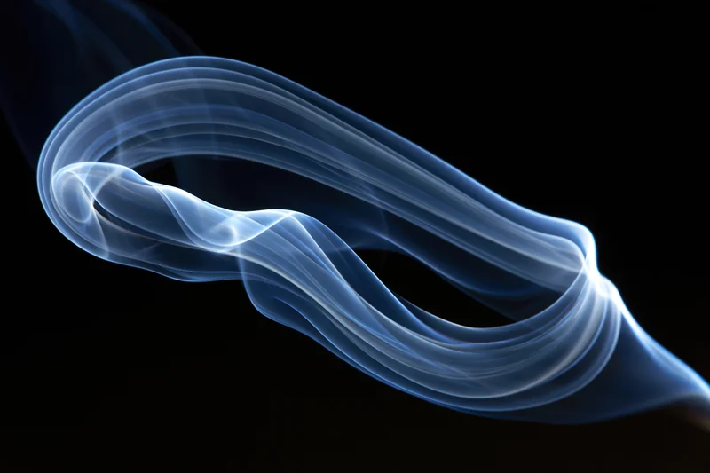 Thin wisp of incense smoke curling into a looping swirl against black background