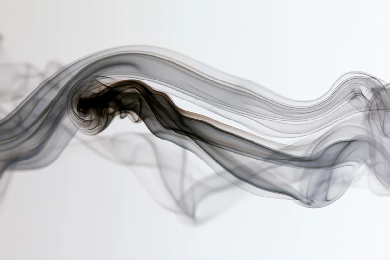 Dark smoke curling and flowing in slow motion against a white background