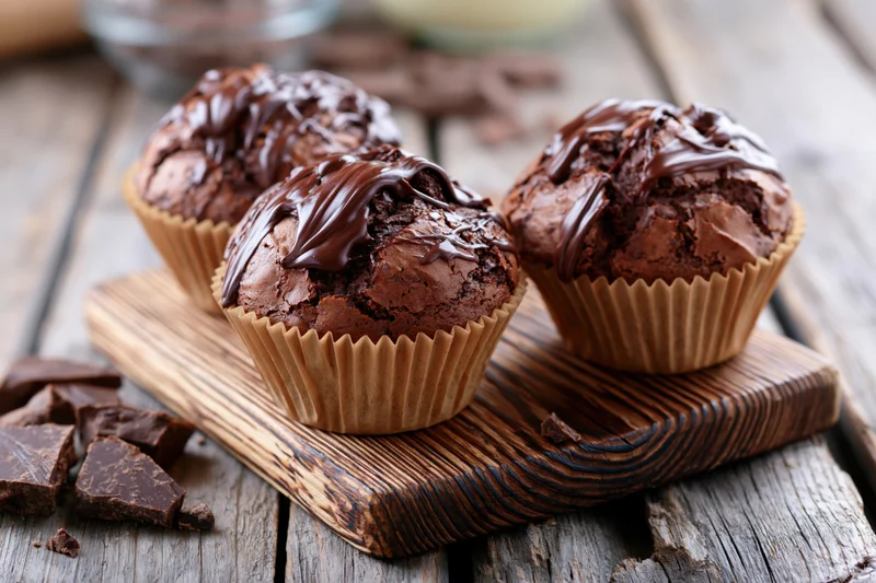 Three chocolate muffins with chocolate glaze on a wooden board