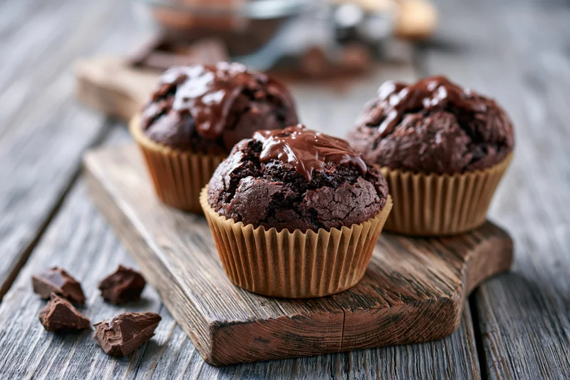 Three muffins in brown paper liners resting on a wooden board