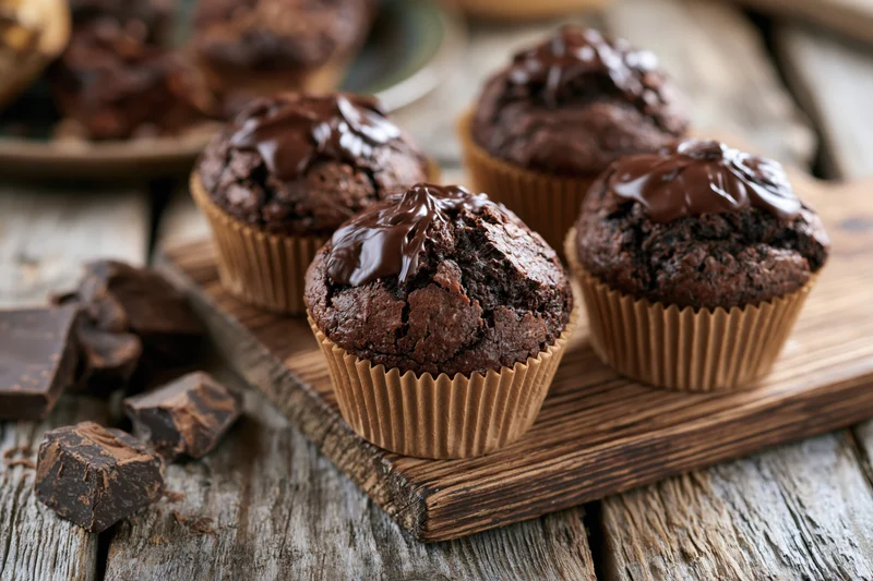 Three chocolate muffins in brown paper liners resting on board