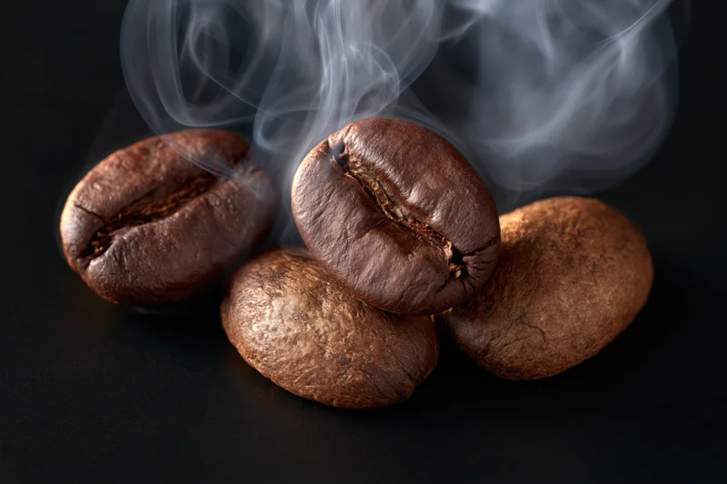 Three roasted coffee beans clustered with wisps of steam