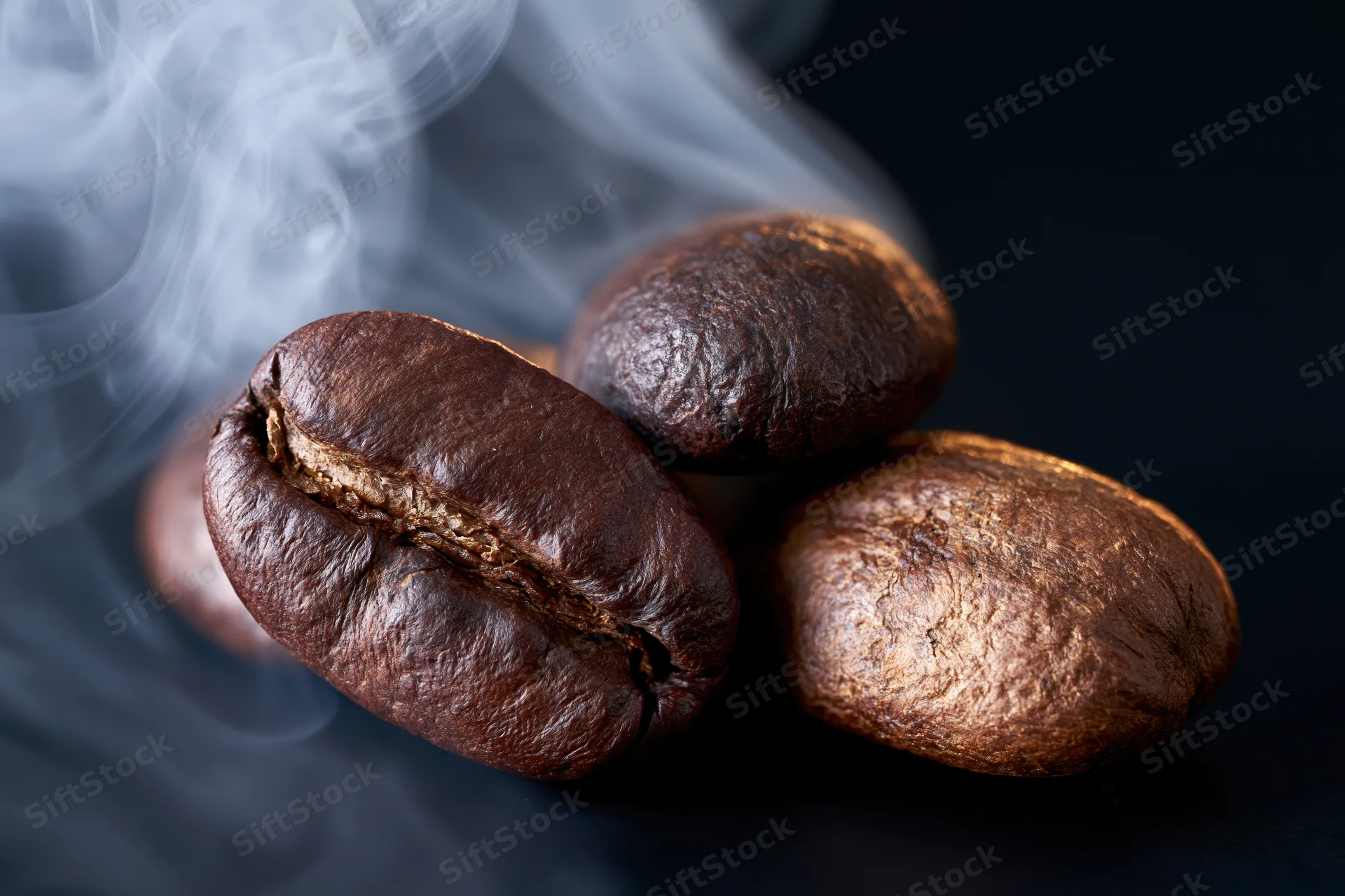 Roasted coffee beans with rising steam on dark surface