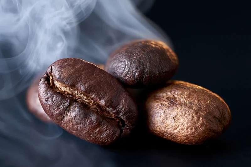 Roasted coffee beans with rising steam on dark surface