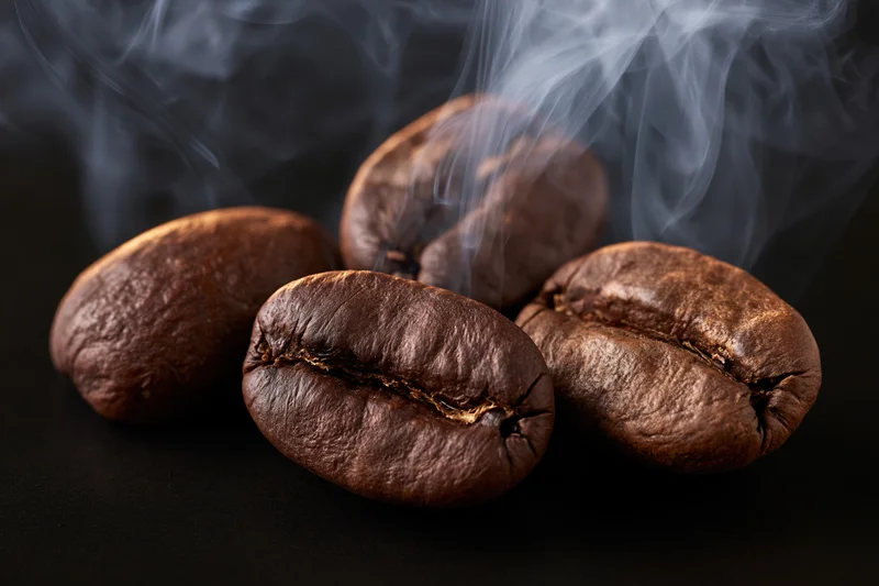 Freshly roasted coffee beans emitting steam on a dark surface