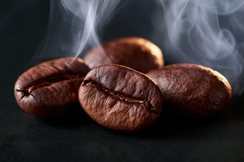 Roasted coffee beans with rising steam on dark surface