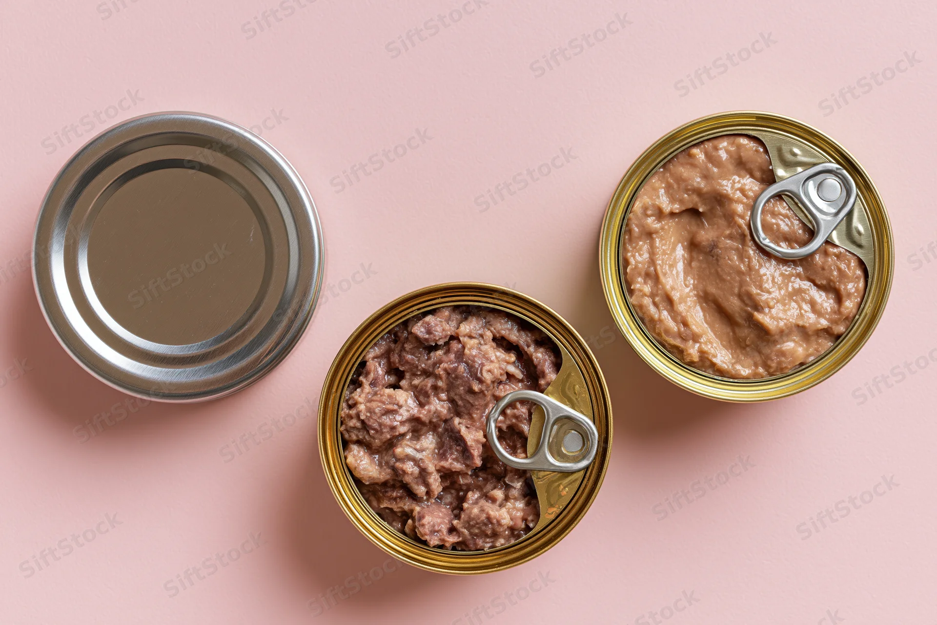 Three open pull-tab cans of wet pet food arranged on a pink surface in flat lay view