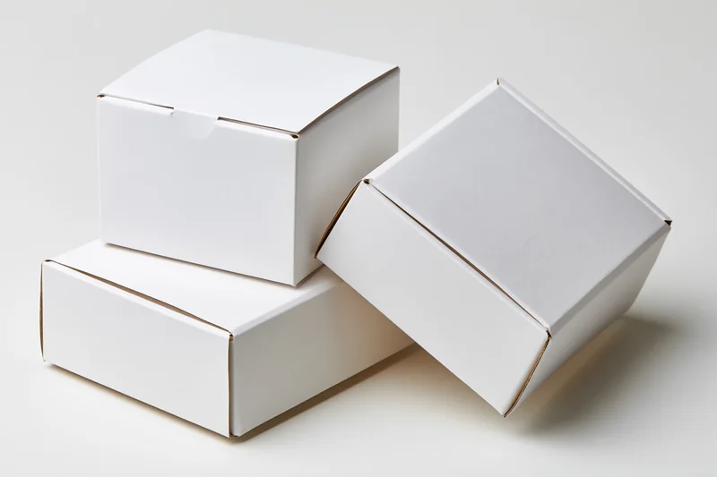 Three plain white cardboard boxes arranged in a casual stack on a white surface