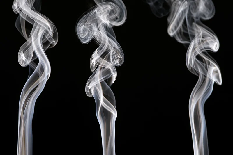 Three white smoke wisps rising and curling upward against a black background