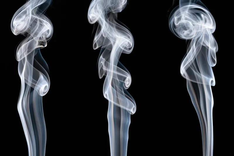 Three white smoke wisps rising and curling upward against a black background