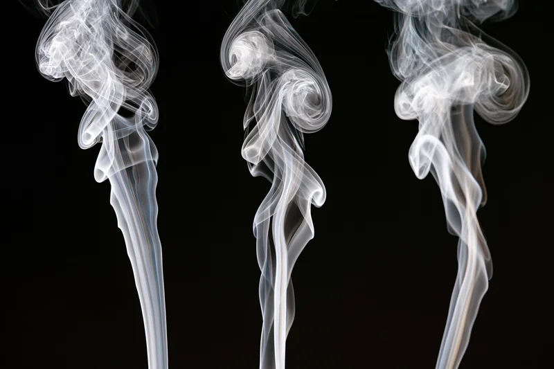 Three white smoke wisps rising and curling upward against a black background