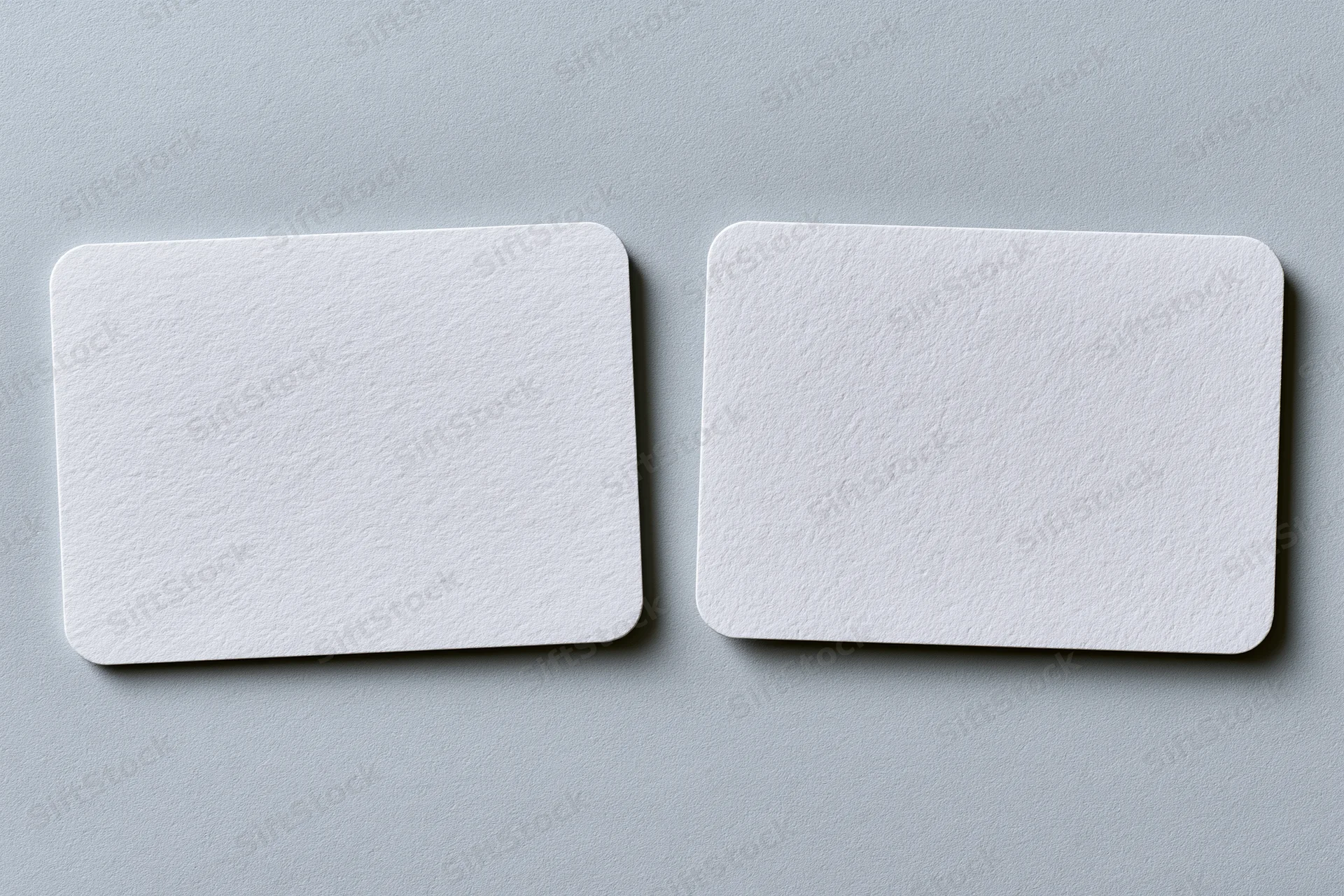 Two blank white textured business cards lying flat side by side on a gray surface