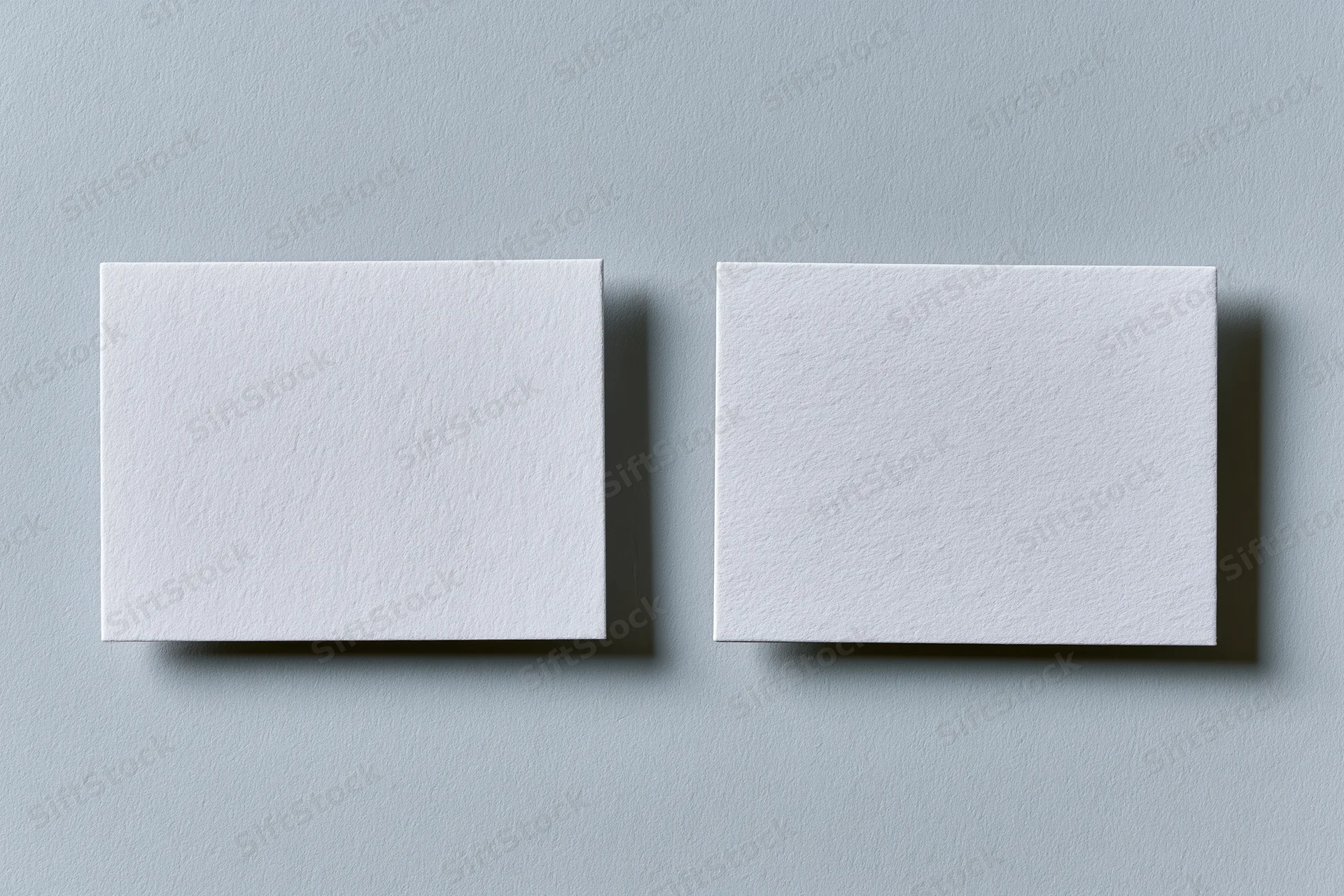 Two blank white textured business cards lying flat side by side on a gray surface