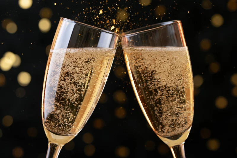 Two champagne flutes clinking together in a toast with golden sparkles against a dark background