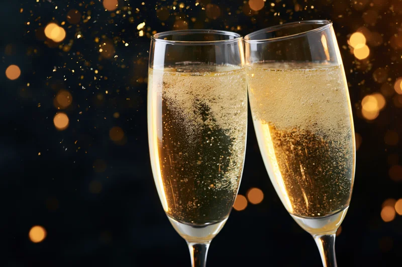 Two champagne flutes clinking together in a toast against a sparkling golden bokeh background