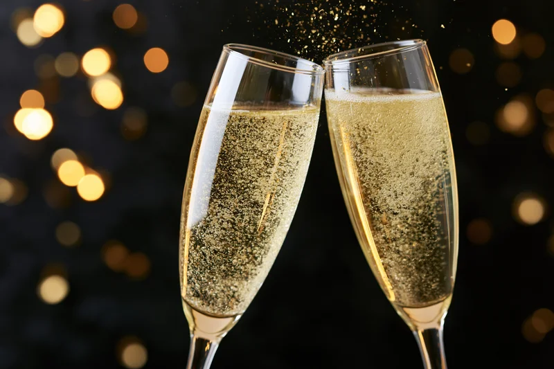 Two champagne flutes clinking together in a toast with golden bubbles and bokeh lights in the background