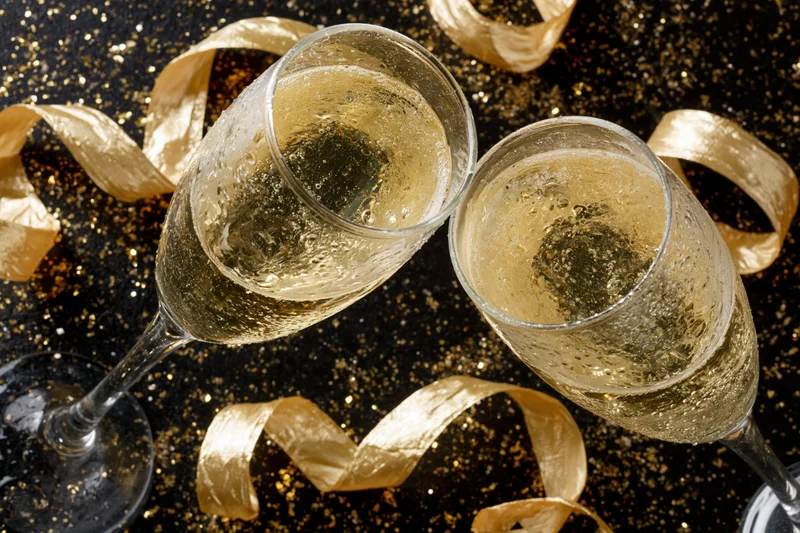 Two champagne flutes clinking together on a black glittery surface with golden ribbons