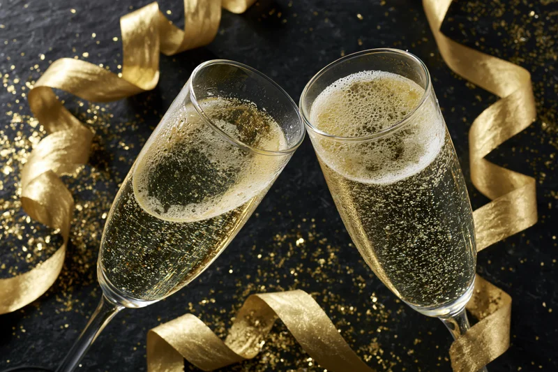 Two champagne flutes clinking together on a black surface with golden ribbons and glitter