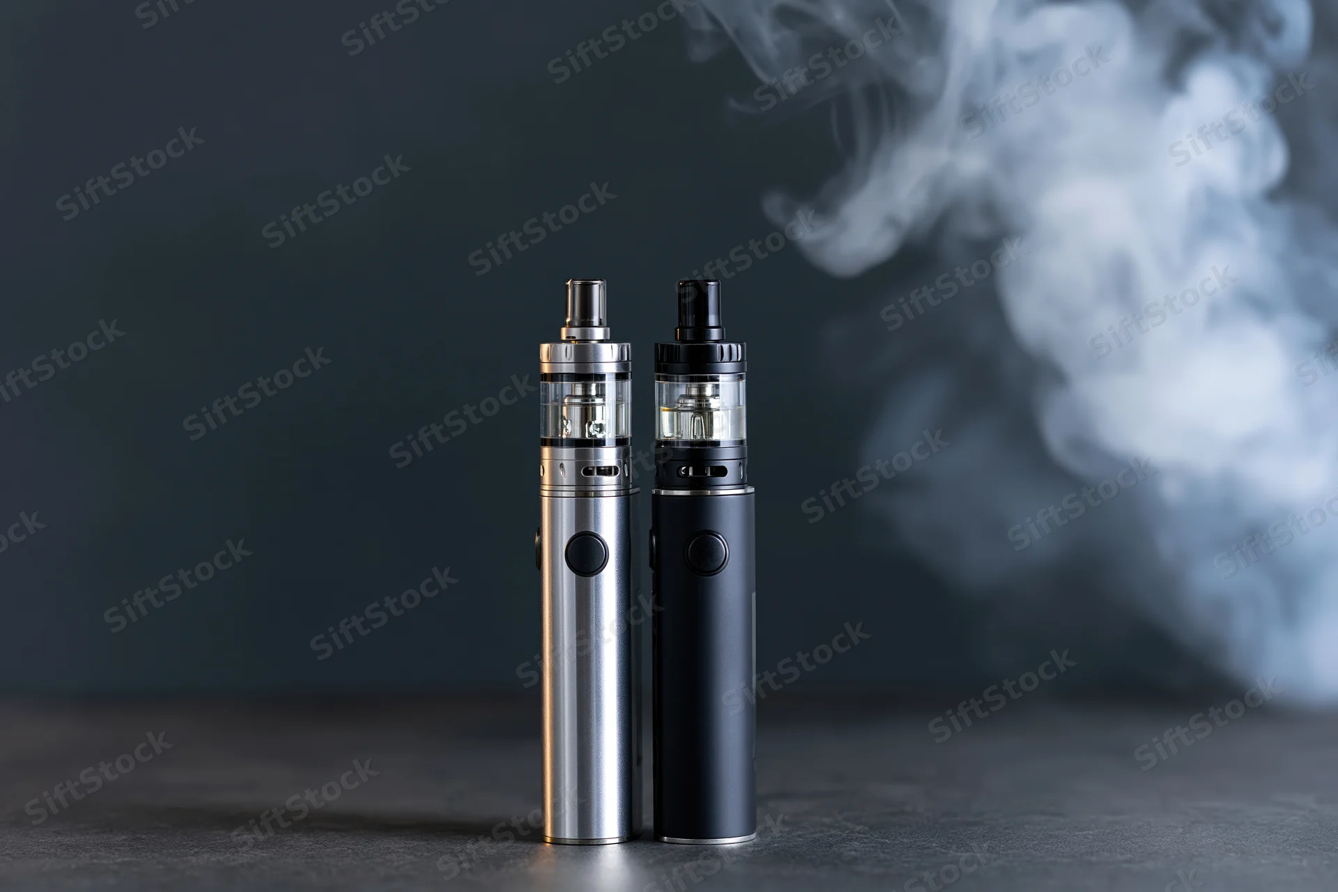 Two vape mods standing side by side on a dark matte surface with vapor in the background