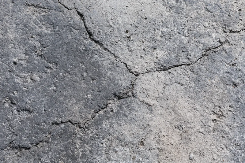 Cracked weathered concrete surface showing diagonal fissures and wear from outdoor exposure