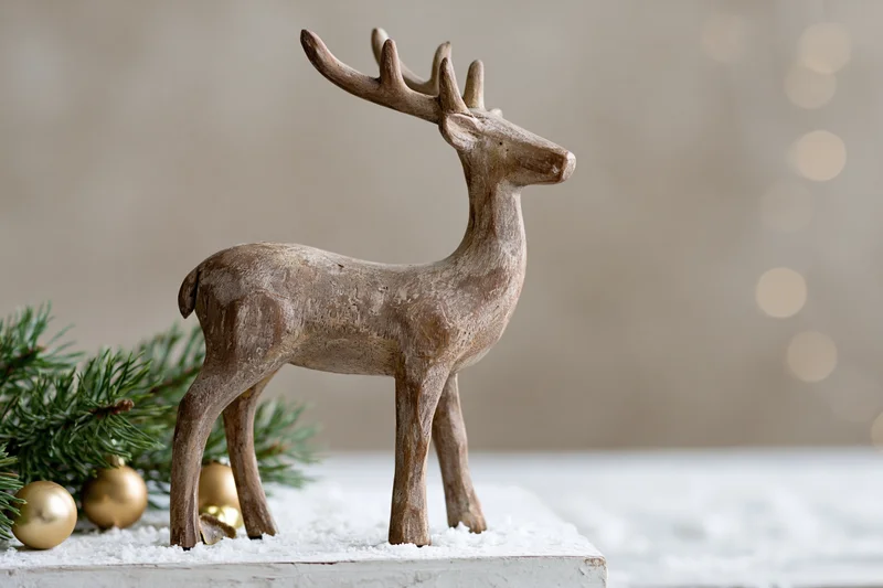 Weathered wooden reindeer figurine standing on snowy surface beside pine branches and gold ornaments