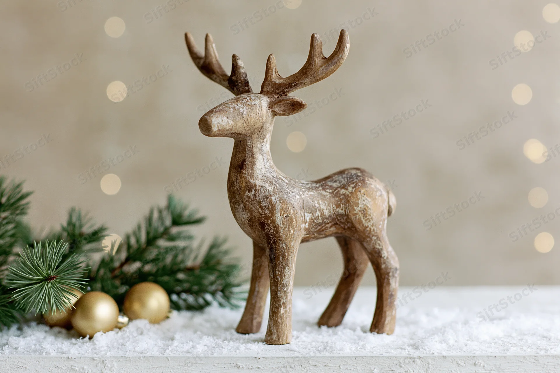 Weathered wooden reindeer figurine standing on snowy surface beside pine branches and golden ornaments