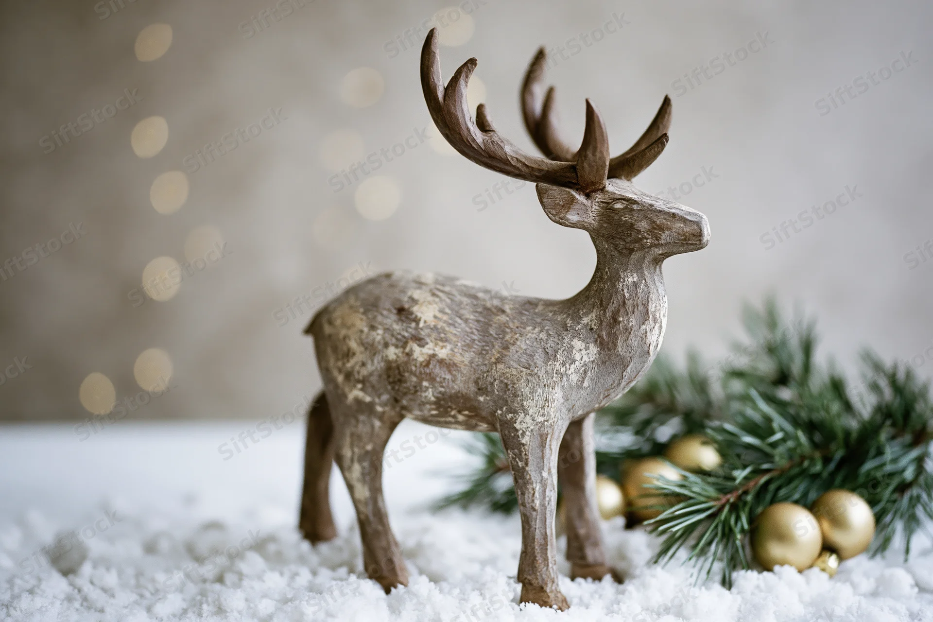 Weathered wooden reindeer figurine standing on snow beside pine branches and gold ornaments with bokeh lights in background