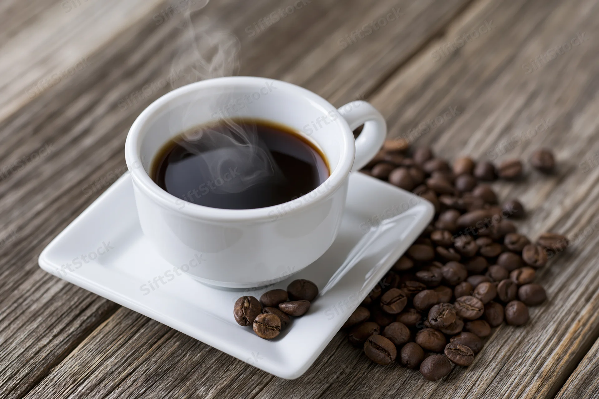Steaming coffee in a white ceramic cup on a square saucer with roasted beans scattered on a wooden table