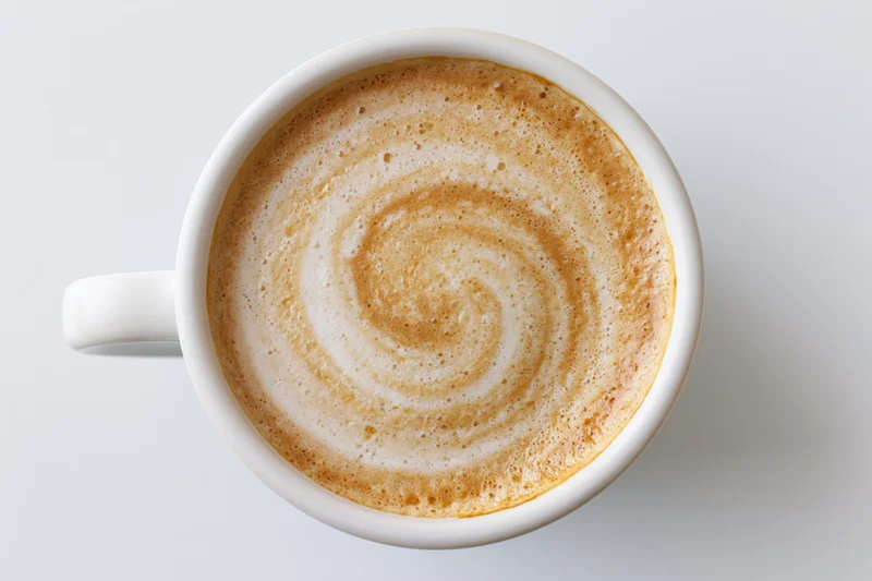 White ceramic coffee cup filled with latte foam swirl viewed from directly above on plain surface