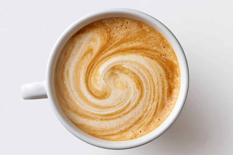 Overhead view of a white ceramic coffee cup filled with latte art swirl on a plain white surface