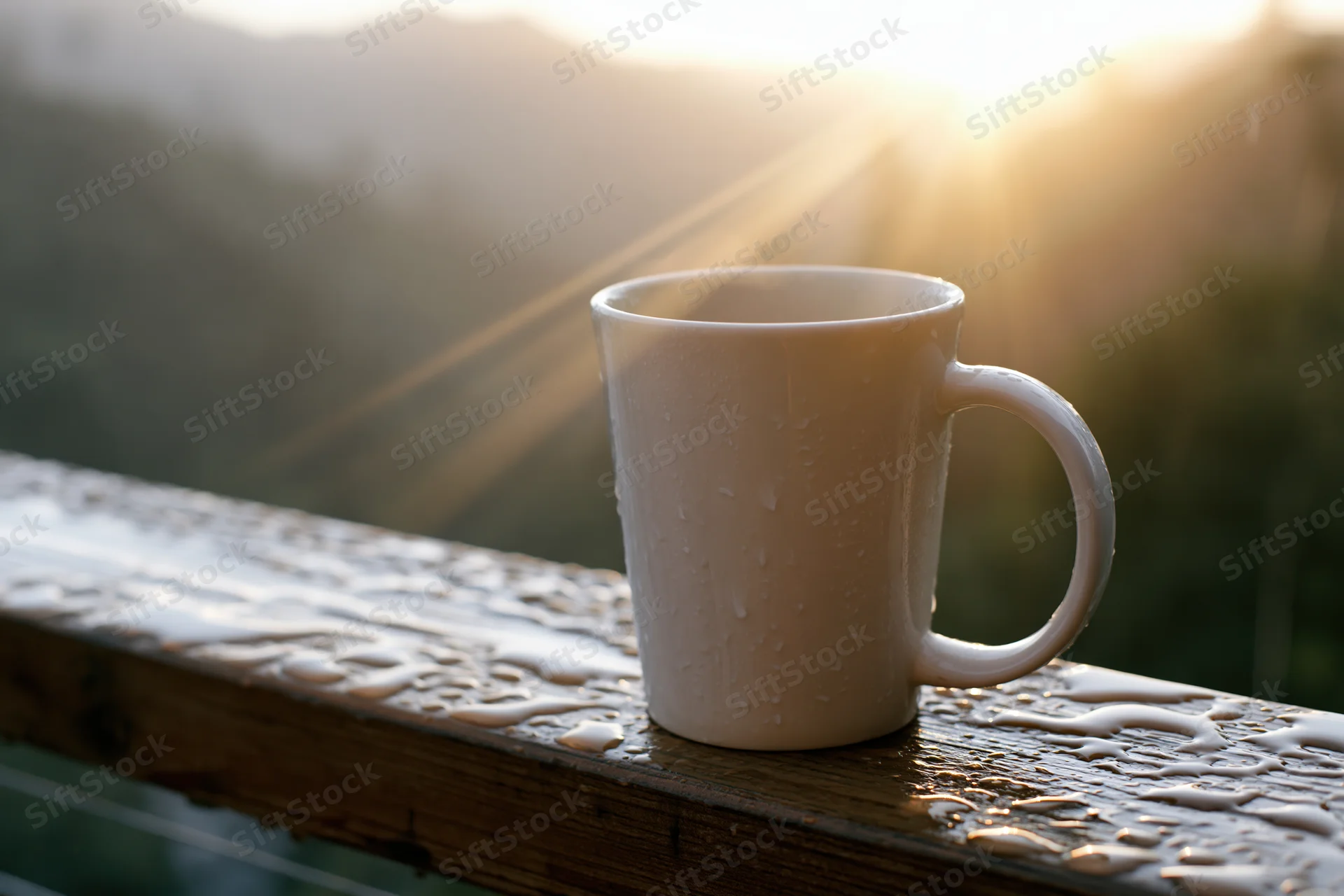 White ceramic coffee mug with water droplets on wet wooden railing at sunrise overlooking mountains