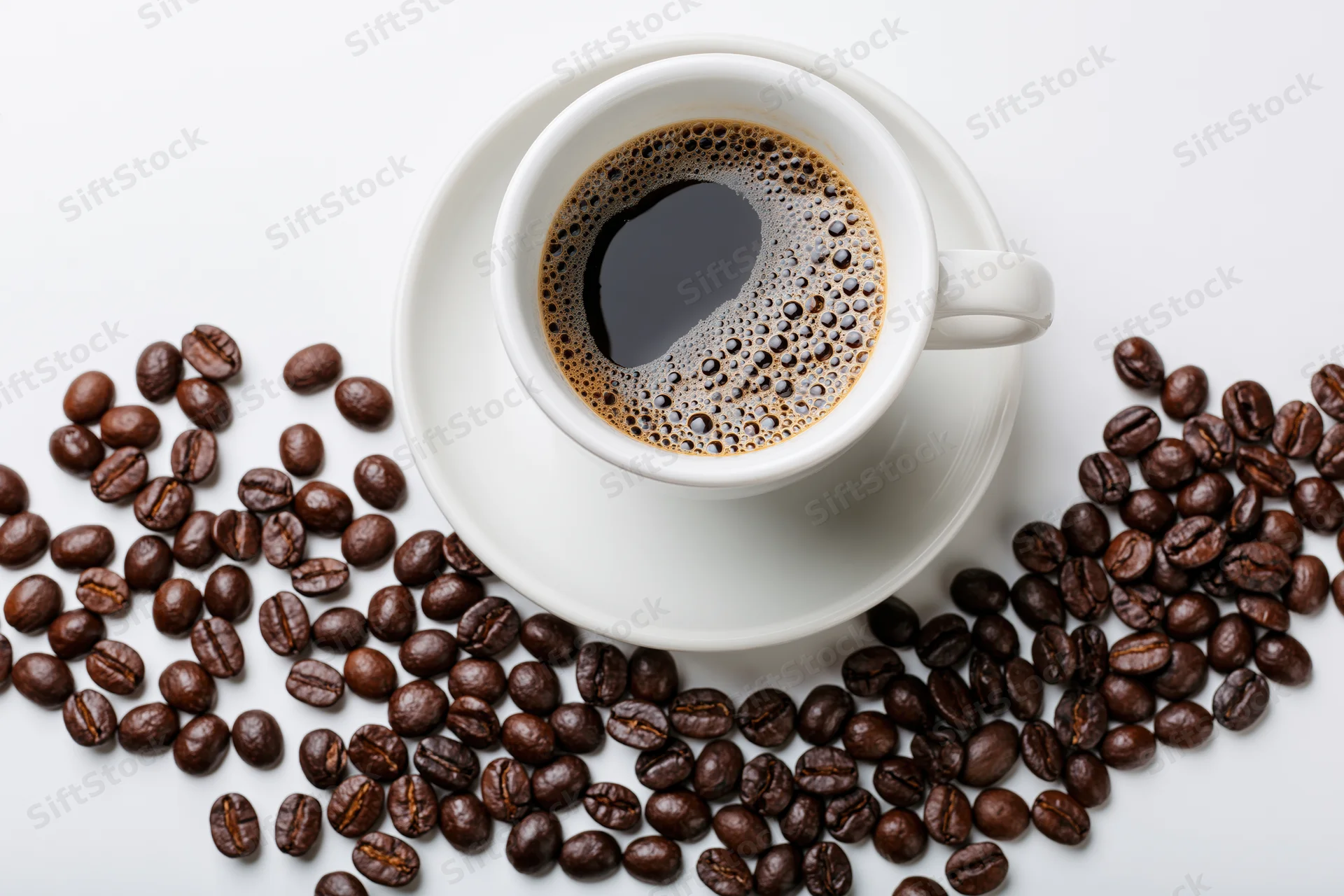 White ceramic cup of black coffee with crema on saucer surrounded by roasted coffee beans on white surface