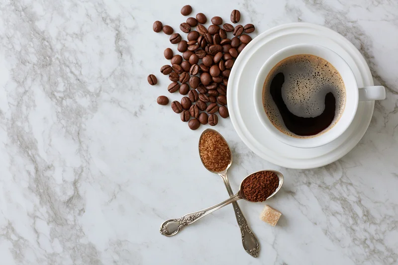 White ceramic coffee cup with foam and coffee beans on marble surface