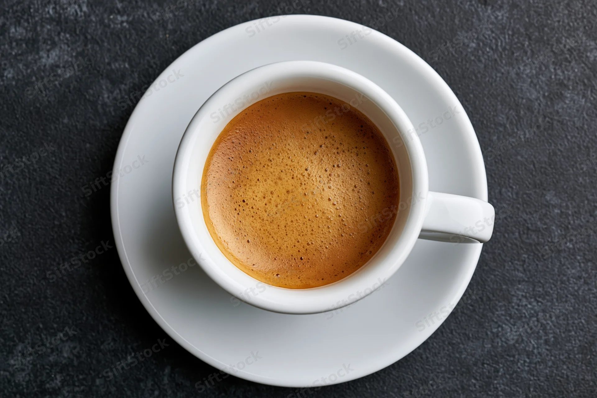 White ceramic espresso cup with frothy crema on dark stone surface, top view