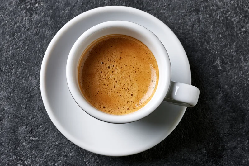 White ceramic espresso cup with crema on dark stone surface, top view