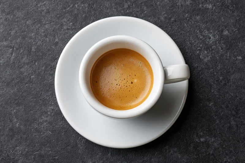 White ceramic espresso cup with crema on dark stone surface, top view