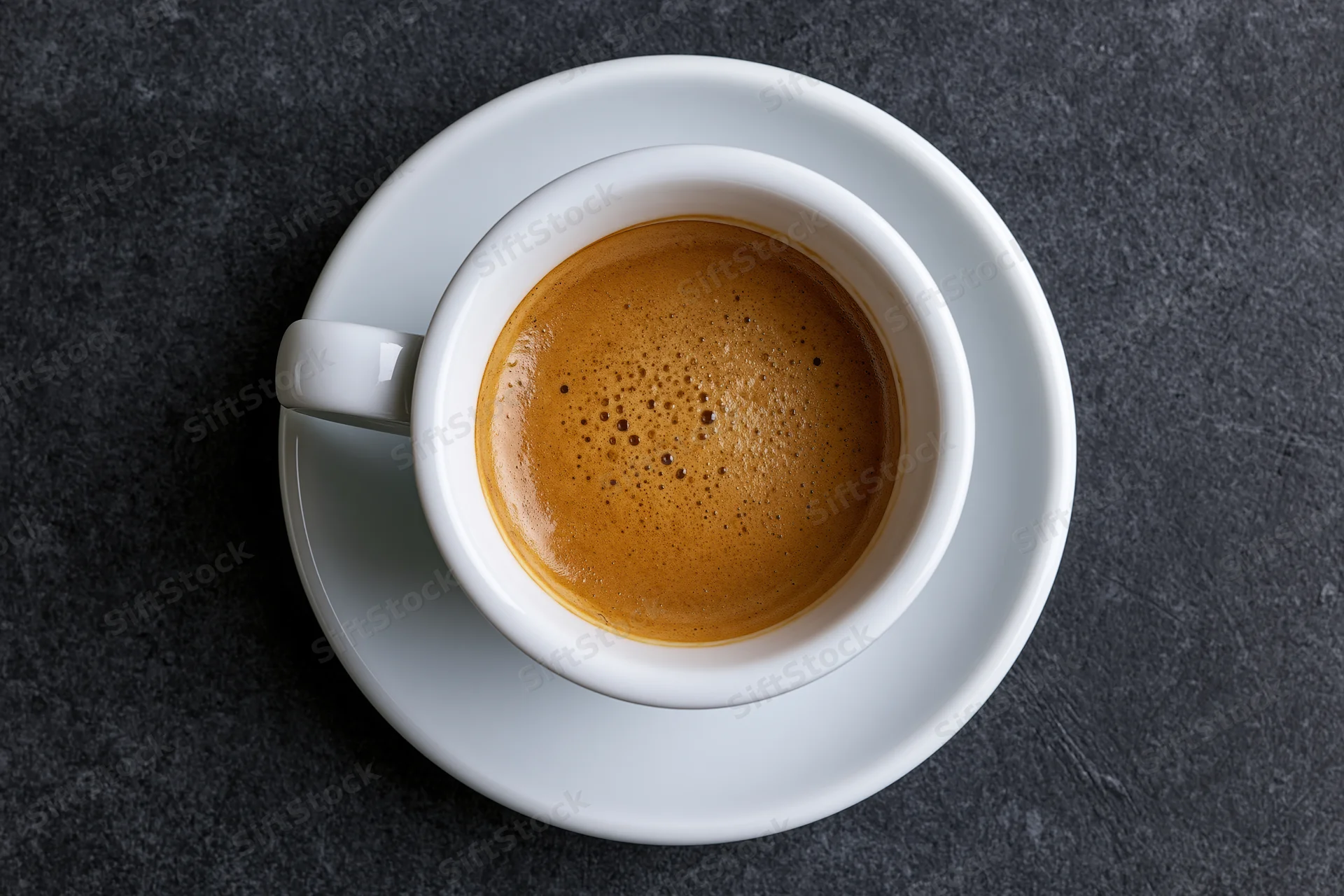 White ceramic espresso cup with crema on dark stone surface, top view