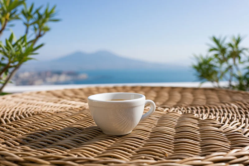 White ceramic espresso cup on woven rattan table overlooking sea and mountains
