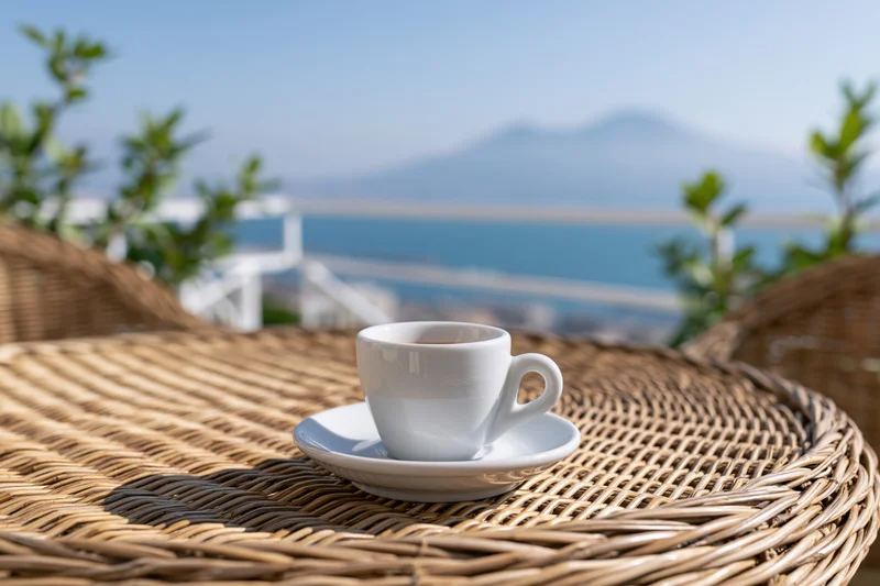 White ceramic espresso cup on a woven rattan table overlooking the sea and mountains