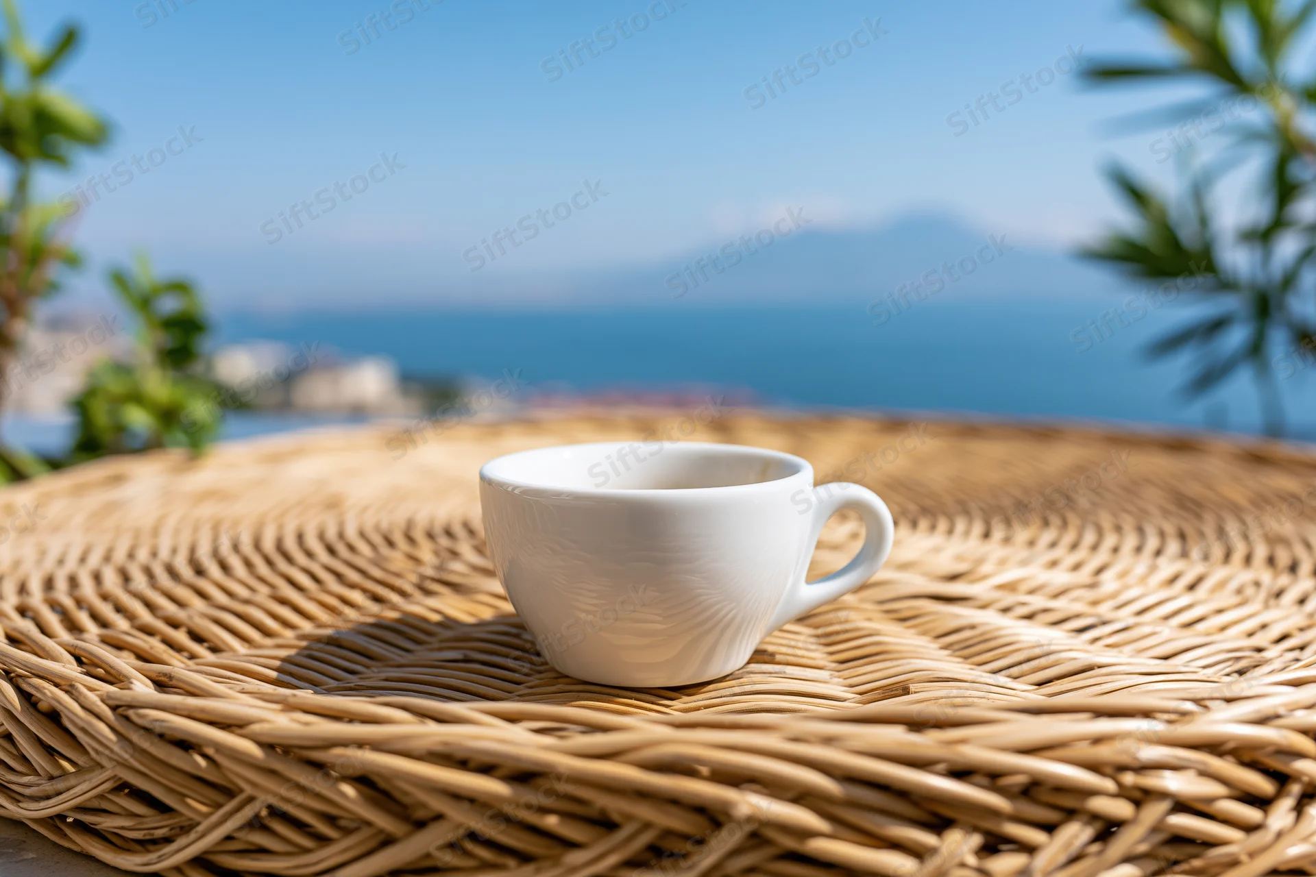 White ceramic espresso cup on woven rattan table overlooking ocean and mountains