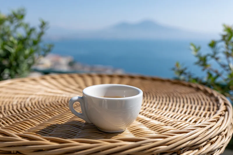 White ceramic espresso cup on a woven rattan table overlooking the sea