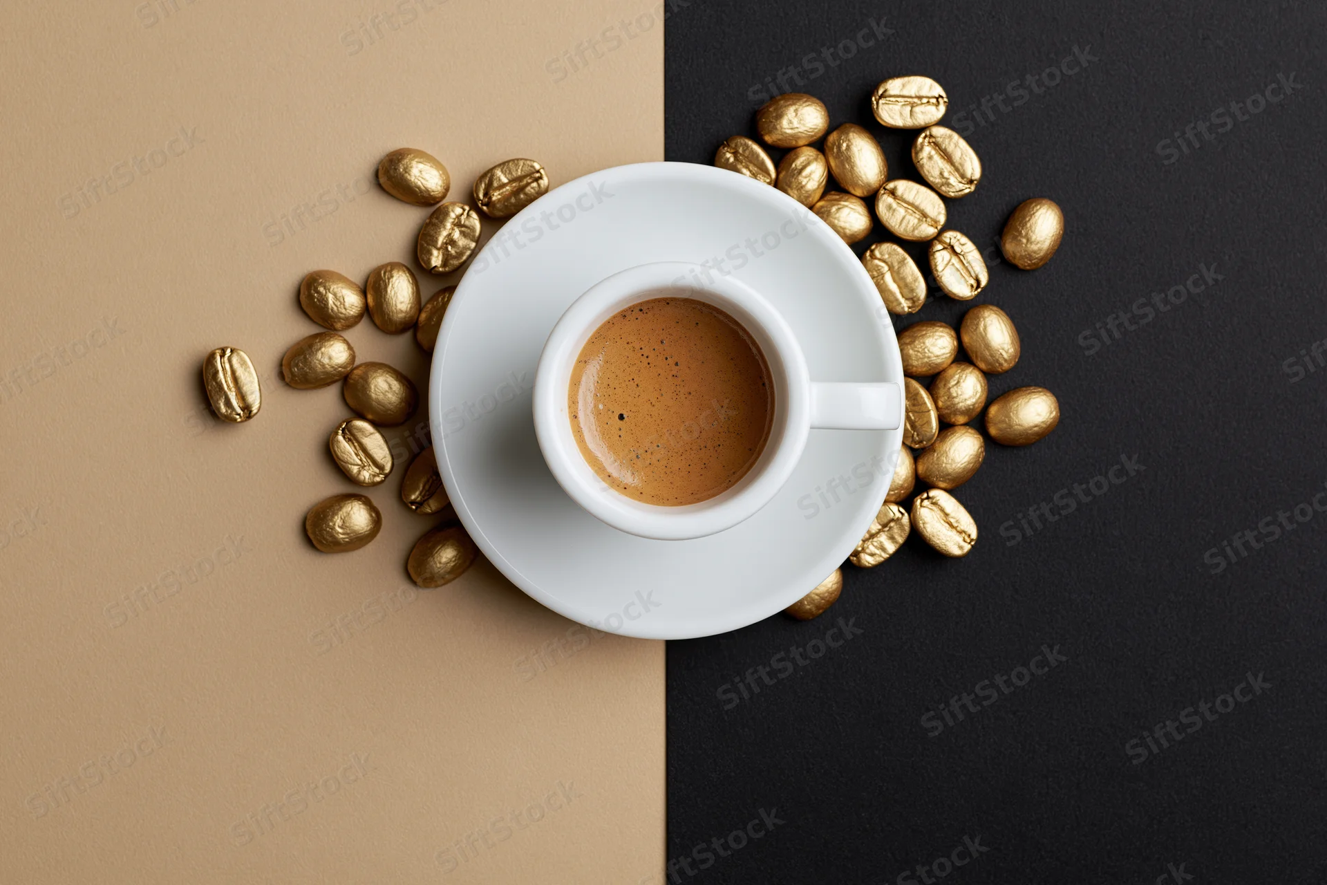 White ceramic espresso cup filled with coffee on saucer surrounded by golden coffee beans on split beige and black background