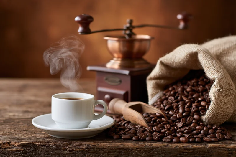 Steaming espresso cup beside roasted coffee beans and vintage grinder on wooden table
