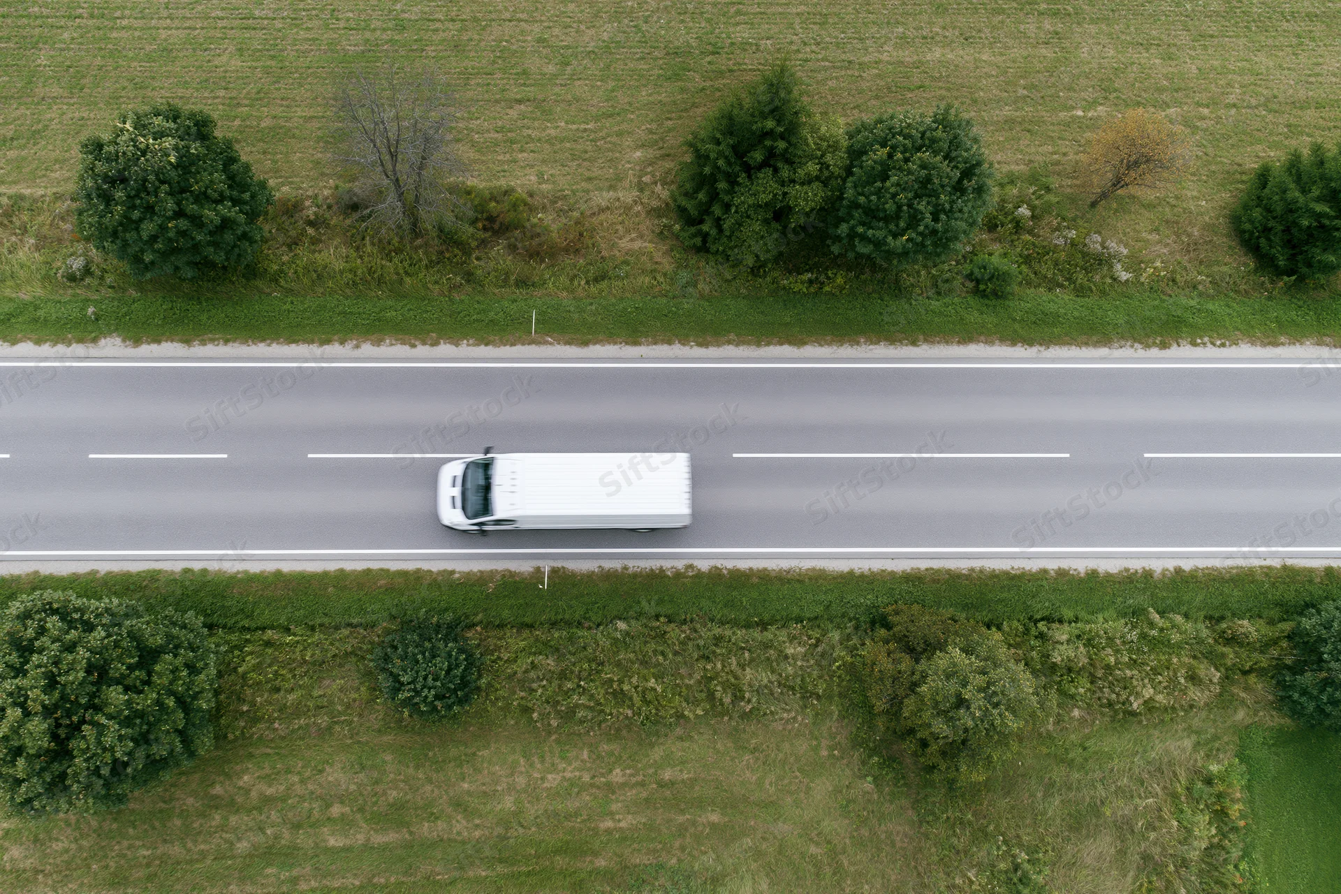 White delivery van driving on a straight rural road viewed from above