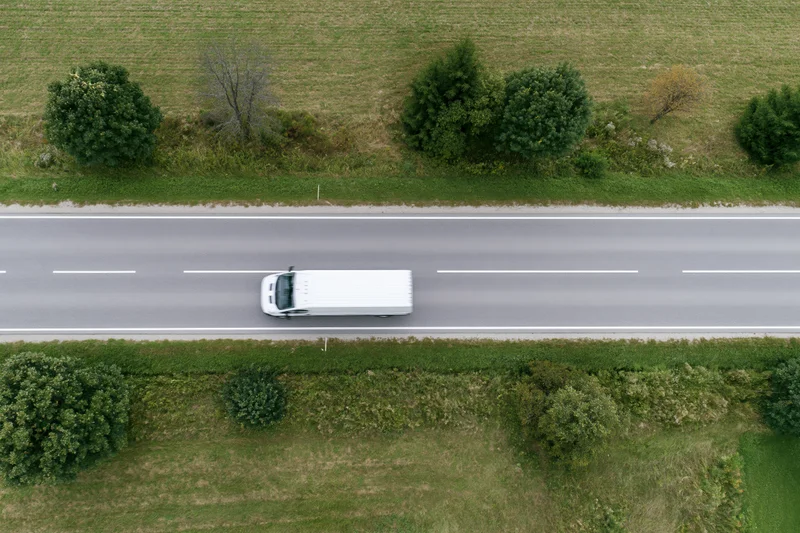 White delivery van driving on a straight rural road viewed from above