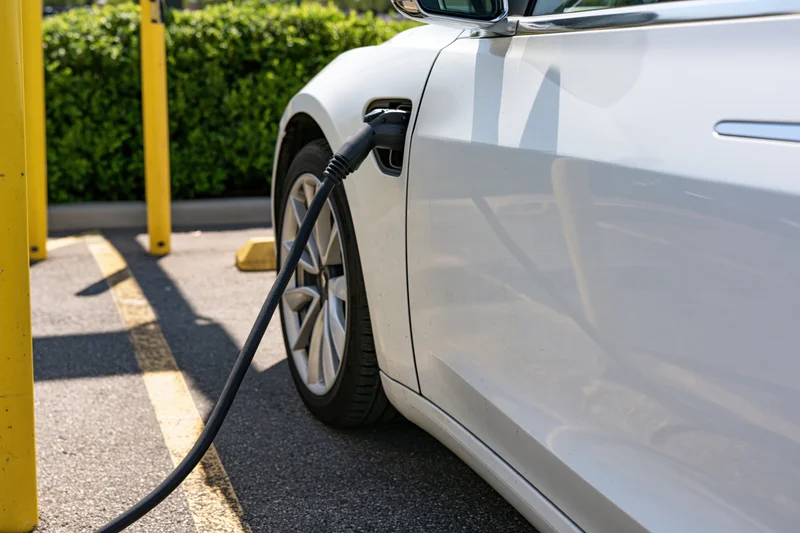 White electric car plugged into charging station in outdoor parking area