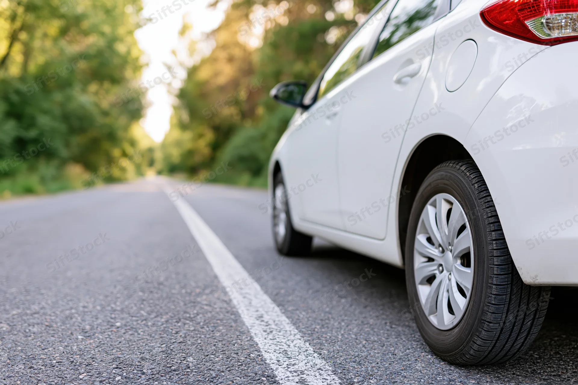 White hatchback parked on the right side of a two-lane country road lined with trees
